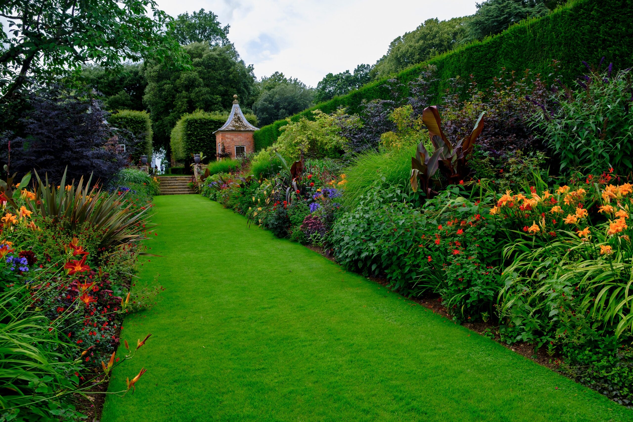 Established flowering borders and clipped hedges framing a grass garden path